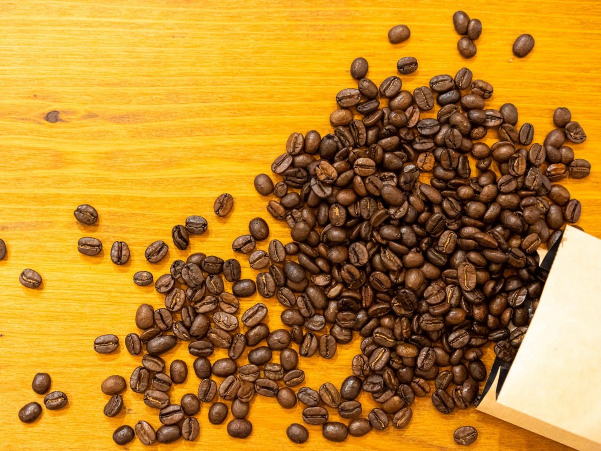 Granos de café tostado saliendo de una bolsa kraft
