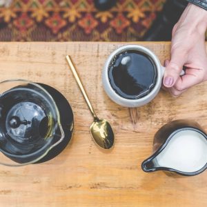Prensa francesa, taza de café y lechera sobre una mesa de madera
