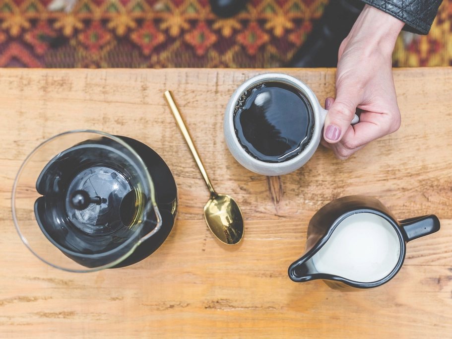 Prensa francesa, taza de café y lechera sobre una mesa de madera